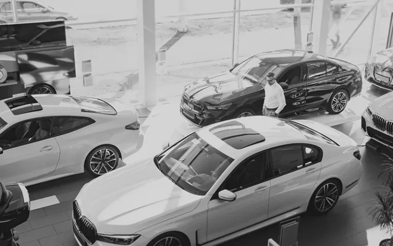 Man walking through a BMW dealership showroom with white and black sedans on display